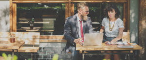 smartly dressed man and woman sat on outdoor bench using laptop