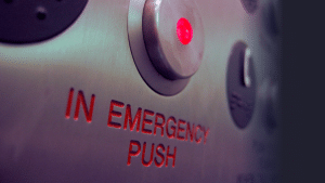 Close‑up of a lift emergency call button with red illumination, indicating an emergency communication system
